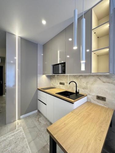 a kitchen with white cabinets and a wooden counter top at Сучасні апартаменти в новобудові in Lviv