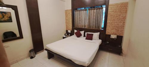 a bedroom with a bed with white sheets and red pillows at Hotel Shivam in Pune