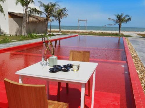 a white table with chairs on a red floor next to the beach at Red Z The Ocean in Phetchaburi