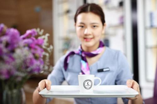 a woman holding a tray with a coffee cup on it at Lavande Hotels·Qingyuan Jinbiwan in Qingyuan