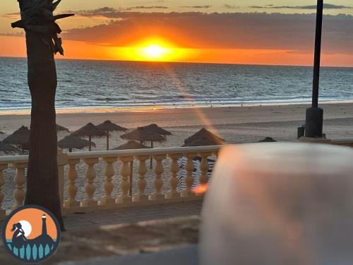 a sunset on a beach with umbrellas and the ocean at Cala Regla by Bossh! Apartments in Chipiona