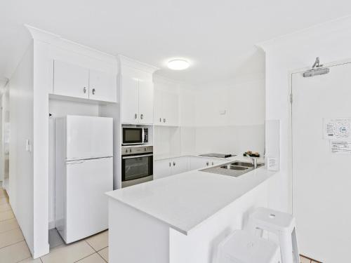 a white kitchen with a refrigerator and a sink at Miami Beachside Holiday Apartments in Gold Coast