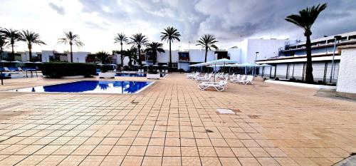 a swimming pool with chairs and umbrellas and palm trees at Casa GABRIEL 1 Bedroom Wifi Free Pool in Costa Del Silencio