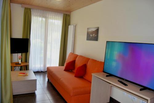 a living room with an orange couch and a flat screen tv at Apartma Bazilika in Topolšica