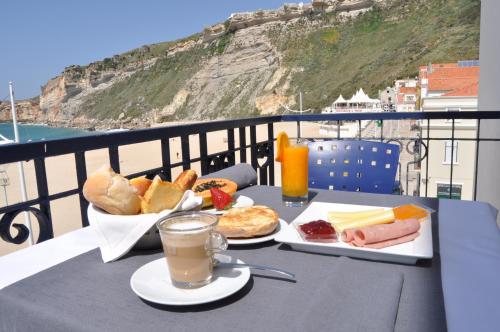 a table with breakfast food and a drink on a balcony at Hotel Mar Bravo in Nazaré