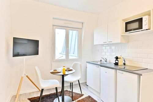 une cuisine avec des armoires blanches et une table et des chaises dans l'établissement Petit Studio chaleureux en Banlieue - Asnières, à Asnières-sur-Seine