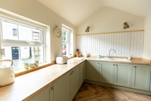 a kitchen with white cabinets and a sink and two windows at OLD BANK HOUSE - Perfect Getaway for Friends & Families in Holker