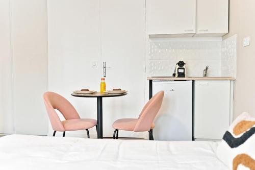 une cuisine avec deux chaises roses et une table dans l'établissement Petit studio équipée en banlieue Parisienne, à Asnières-sur-Seine