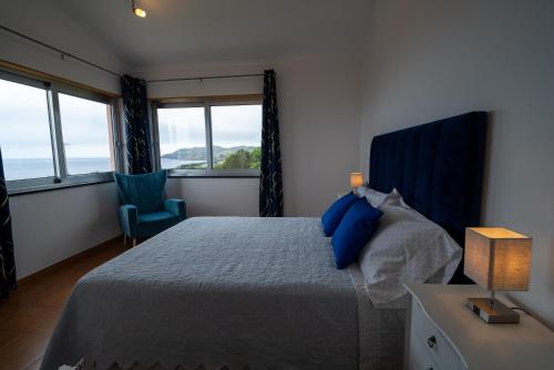 a bedroom with a bed and a chair and windows at Vila Canada das Vinhas in Porto Martins
