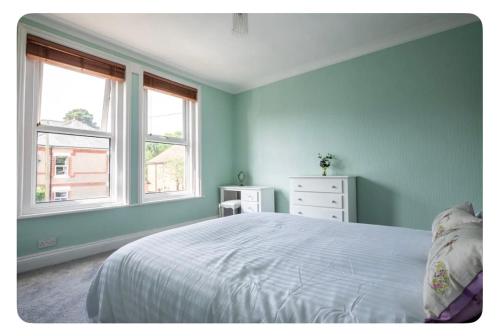 a blue bedroom with a bed and two windows at Beautiful Garden Flat in Bournemouth - First Floor in Bournemouth