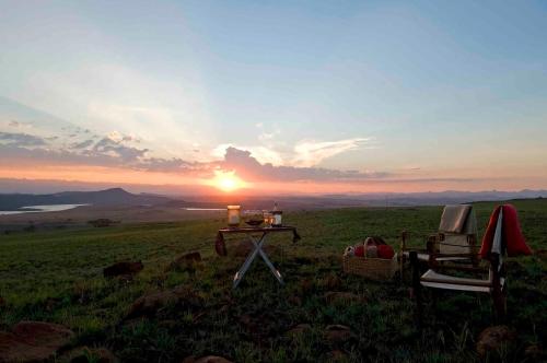 a sunset with a table and chairs in a field at Three Tree Hill Lodge in Bergville