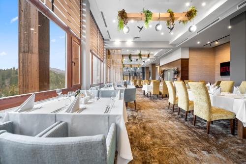 a restaurant with white tables and chairs and large windows at Hotel Orlovetz in Pamporovo