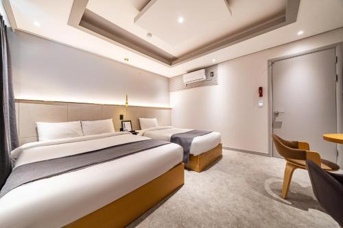 two beds in a hotel room with a table and chairs at Sokcho Ritz Hotel in Sokcho