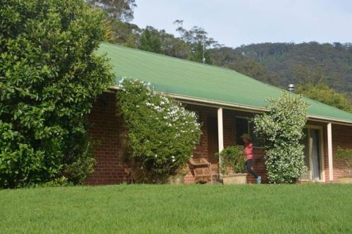 a woman standing outside a brick house with a green roof at Charlie & Roy's Farm Berry in Berry