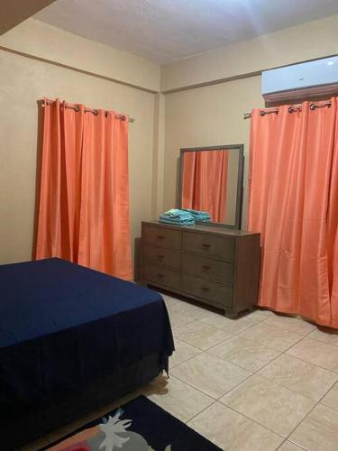 a bedroom with orange curtains and a dresser and a mirror at Windsor Apartment in Kingstown