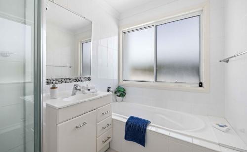 a white bathroom with a tub and a sink and a window at Azul Blue at Shellys in Port Macquarie