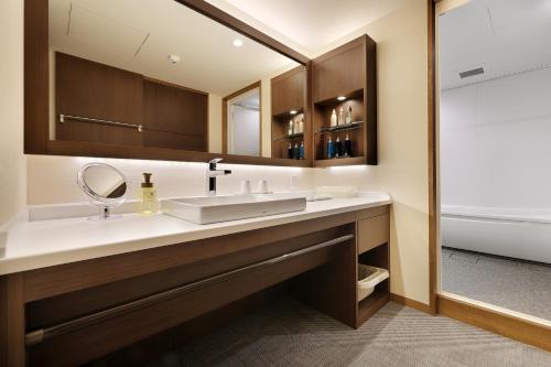 a bathroom with a sink and a mirror and a tub at Zao Kokusai Hotel in Zao Onsen