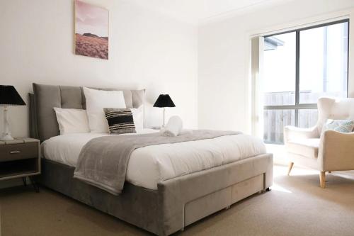 a white bedroom with a large bed and a chair at Kellyvile Delight 5BrHouseParkingShopping Center in Kellyville