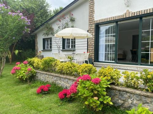a house with a garden with flowers and an umbrella at Casa la Choza, con piscina en la playa de Oriñón in Oriñón