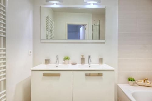 Un baño blanco con lavabo y espejo. en Seaside Serenity Cozy 2-BR Escape, en Blankenberge