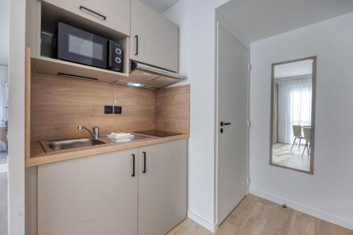 a kitchen with white cabinets and a sink and a mirror at KOSY APPART'HÔTELS - Résidence du Lac in Aix-les-Bains
