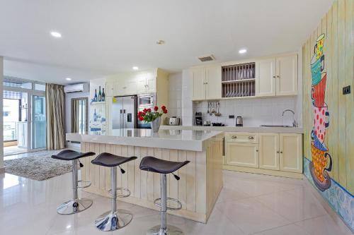 a kitchen with white cabinets and bar stools in it at Grosvenor House - Olympic Pool - Pattaya in Pattaya South