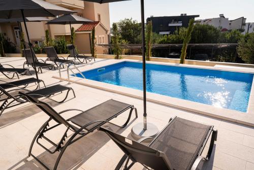 a group of chairs and umbrellas next to a swimming pool at Villa Full Moon Luxury Apartments Novalja in Novalja
