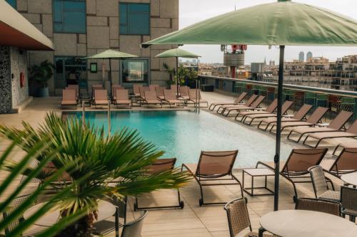a pool on the roof of a building with chairs and an umbrella at Catalonia Barcelona Plaza in Barcelona
