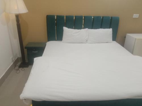 a bed with white sheets and a green headboard at Victoria Guest House in Bahawalpur