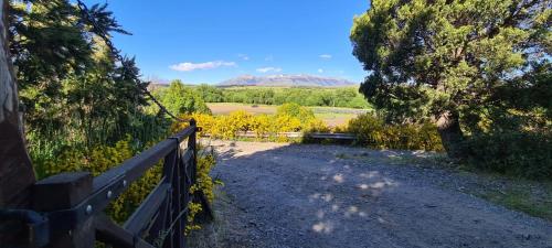 a fence on a dirt road with trees and mountains at Criollo Restó & Cabañas in Trevelin