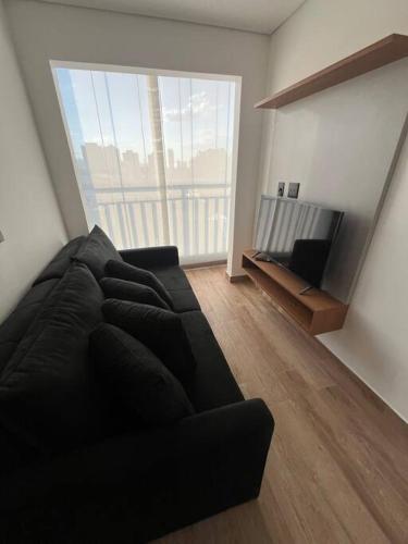 a living room with a black couch and a large window at Apt próximo do metrô carrão in Sao Paulo