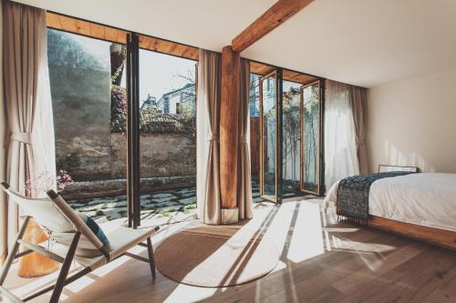 a bedroom with a bed and a chair and large windows at Infini House in Dali