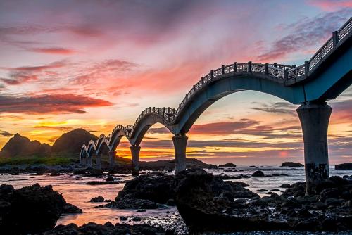 a bridge over the water with a sunset in the background at 幸福有約民宿 in Hsing-ch'ang