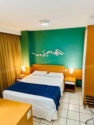 a bedroom with a large bed and a green wall at Praia do Canto Apart Hotel - Quarto sala e varanda in Vitória