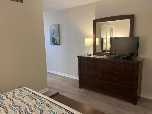 a bedroom with a dresser with a television and a mirror at Summer Sands - 307 by Sea Scape Properties in Wrightsville Beach