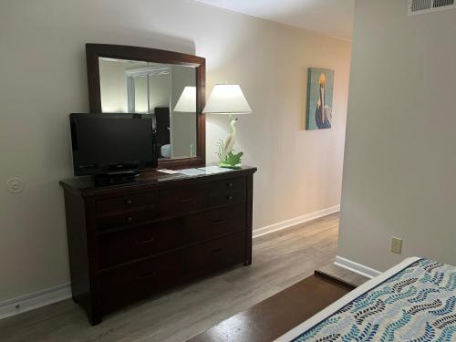 a bedroom with a dresser with a television and a mirror at Summer Sands - 308 by Sea Scape Properties in Wrightsville Beach