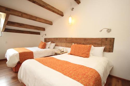 a hotel room with two beds with orange and white sheets at Hotel Ciudad Real Centro Historico in San Cristóbal de Las Casas