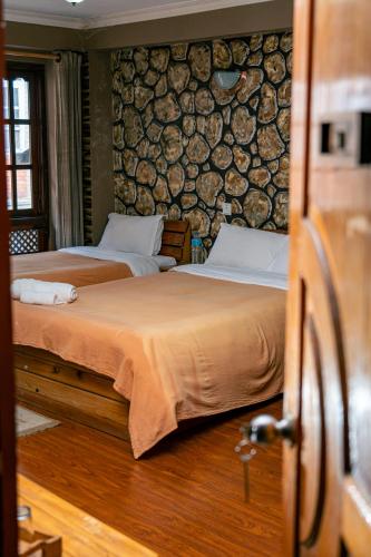 two beds in a room with a wall of logs at City Guest House in Bhaktapur