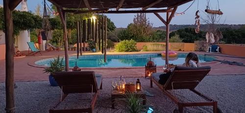 a woman sitting in chairs in front of a pool at Rural Peace in the Algarve - Private Room with kitchenette and bathroom in Aldeia dos Matos