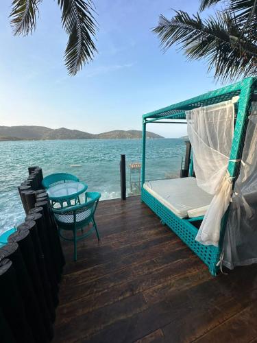 a porch with a bed and a table and the ocean at Pousada Vista Grega in Arraial do Cabo