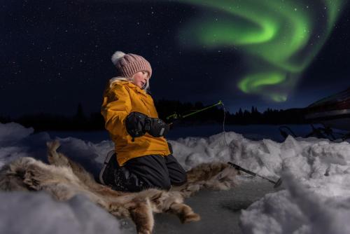 a woman is sitting on a sled in the snow under the aurora at Kiruna Mountain Lodge in Kiruna