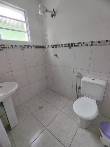 a white bathroom with a toilet and a sink at Suítes Córdoba SP in Bertioga