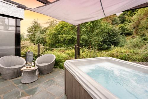a hot tub on a patio with two chairs and an umbrella at Aphrodites Group - Luxury Hot Tub Suites in Central Lake District! in Bowness-on-Windermere