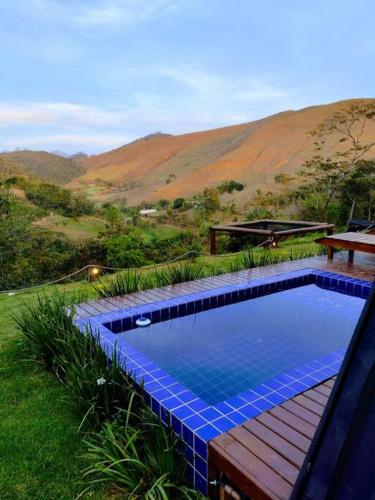 a blue swimming pool with a wooden deck next to a hill at Refúgio dos Alpes cabana in Teresópolis