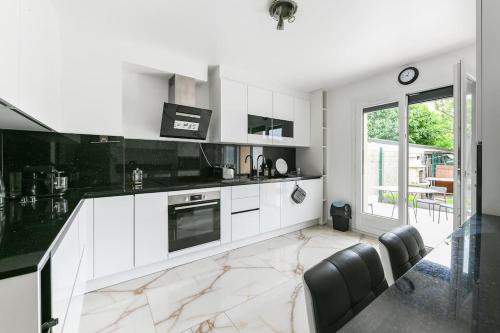 une cuisine avec des armoires blanches et un comptoir noir dans l'établissement L'Elégante Etoile Parisienne avec Terrasse - Proche Gare et Seine, aux Mureaux