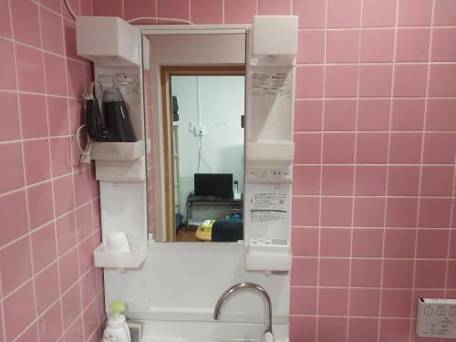 a mirror in a pink tiled bathroom with a sink at 自炊の出来るキッチン付きの貸切宿-Joyjoy奄美 in Setouchi
