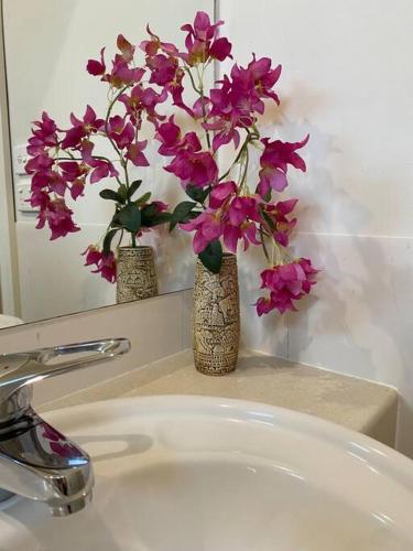 two vases with purple flowers on a bathroom sink at Hidden Hedges - 5 min walk to town in Daylesford
