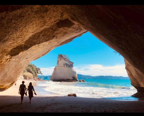 two people walking on a beach with a rock formation at Ridge Valley View in Whenuakite
