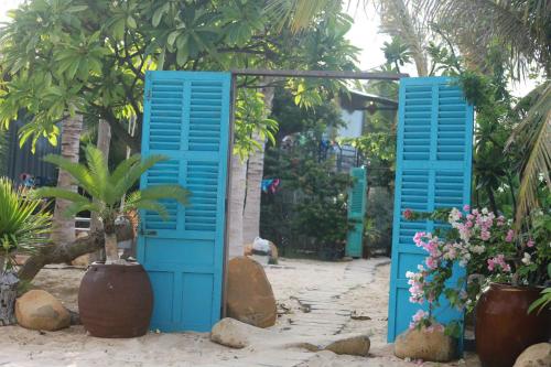 a pair of blue doors in a garden with plants at Hành Ngò Homestay - Hòn Đỏ Ninh Thuận in Thôn Dư Khánh