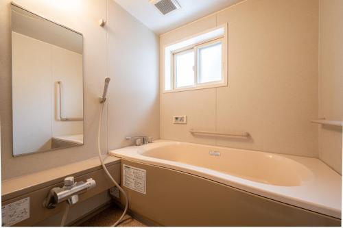 a bathroom with a tub and a window and a sink at Shibuonsen House in Yamanouchi